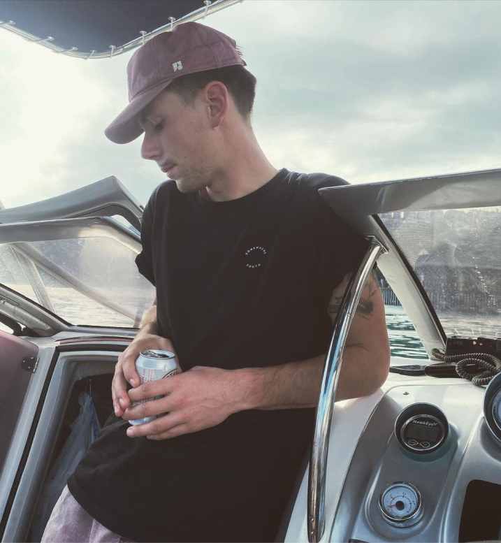 Man on a boat holding a beverage can wearing Somewhere South apparel