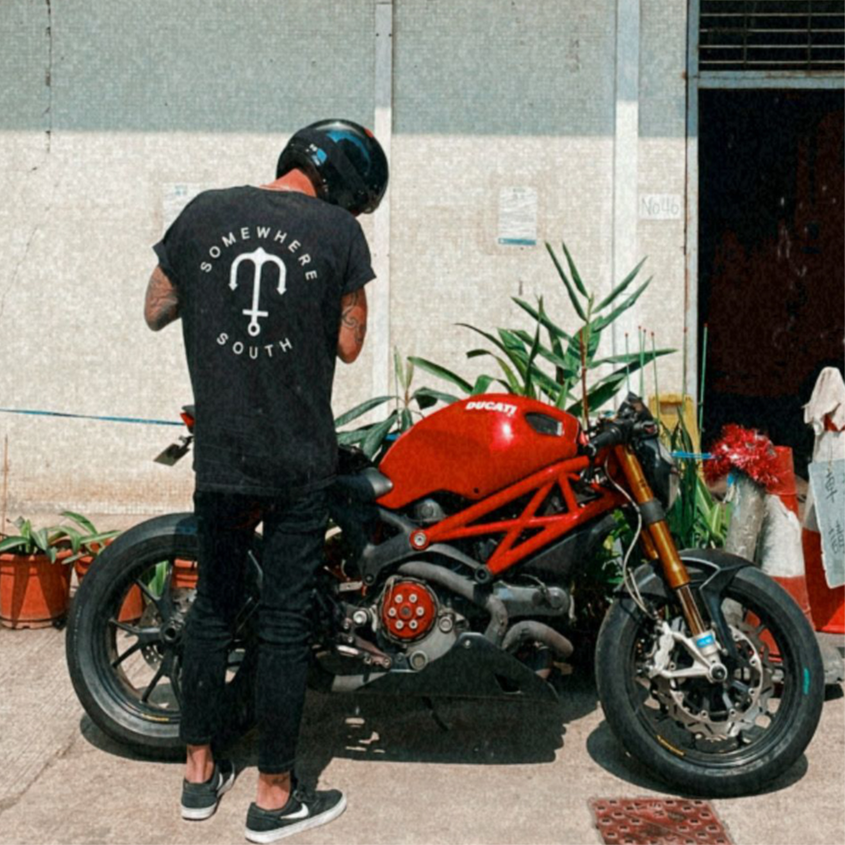 Person in motorcycle helmet wearing Somewhere South anchor logo t-shirt beside a Ducati